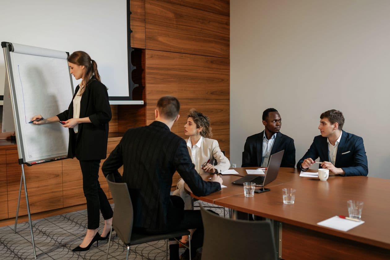 Une formatrice écrit sur un tableau de conférence devant quatre participants assis autour d'une table